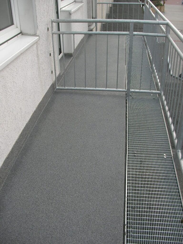 Graue Balkonoberfläche mit Wandanschluss und Metallgeländer.