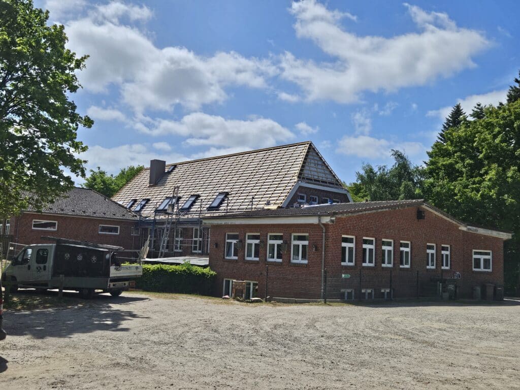 Teilweise abgedecktes Dach eines Backsteingebäudes mit Dachlattung und mehreren Dachfenstern.