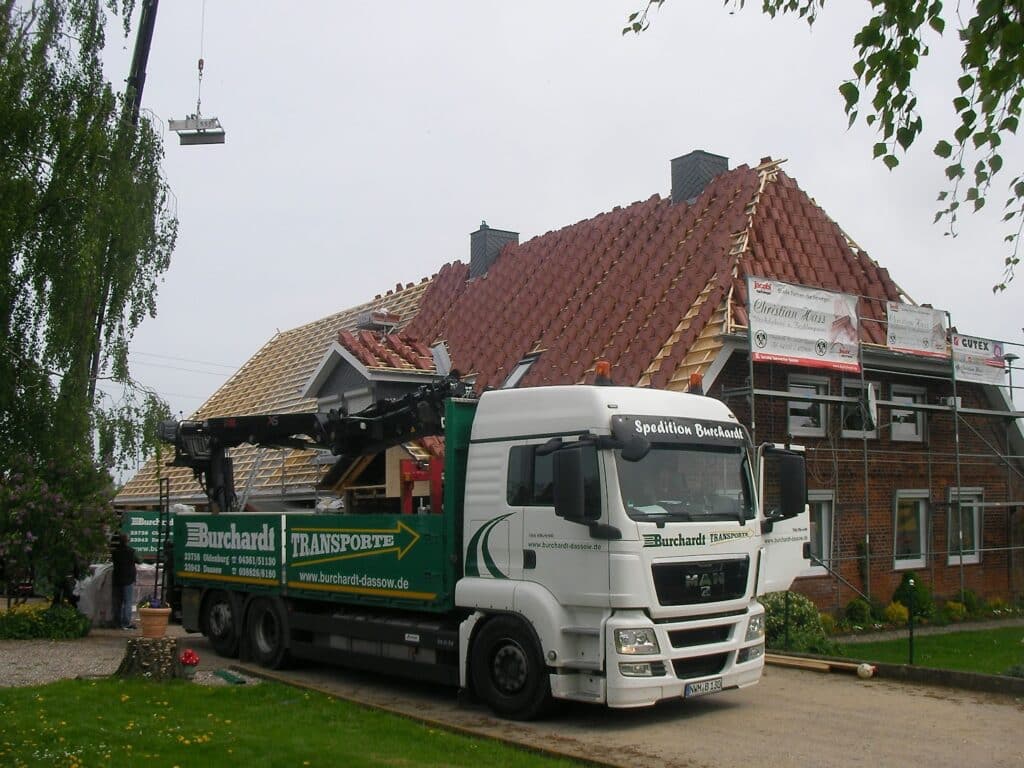 Eingerüstetes Backsteinhaus mit teilweise neu eingedecktem rotem Dach und Baustellenfahrzeug.