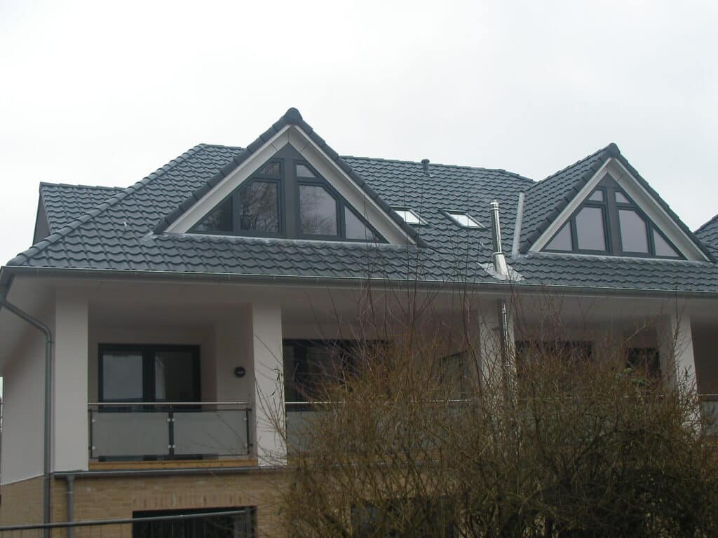 Dunkel gedecktes Hausdach mit zwei Giebelgauben und sichtbaren Holzdetails.
