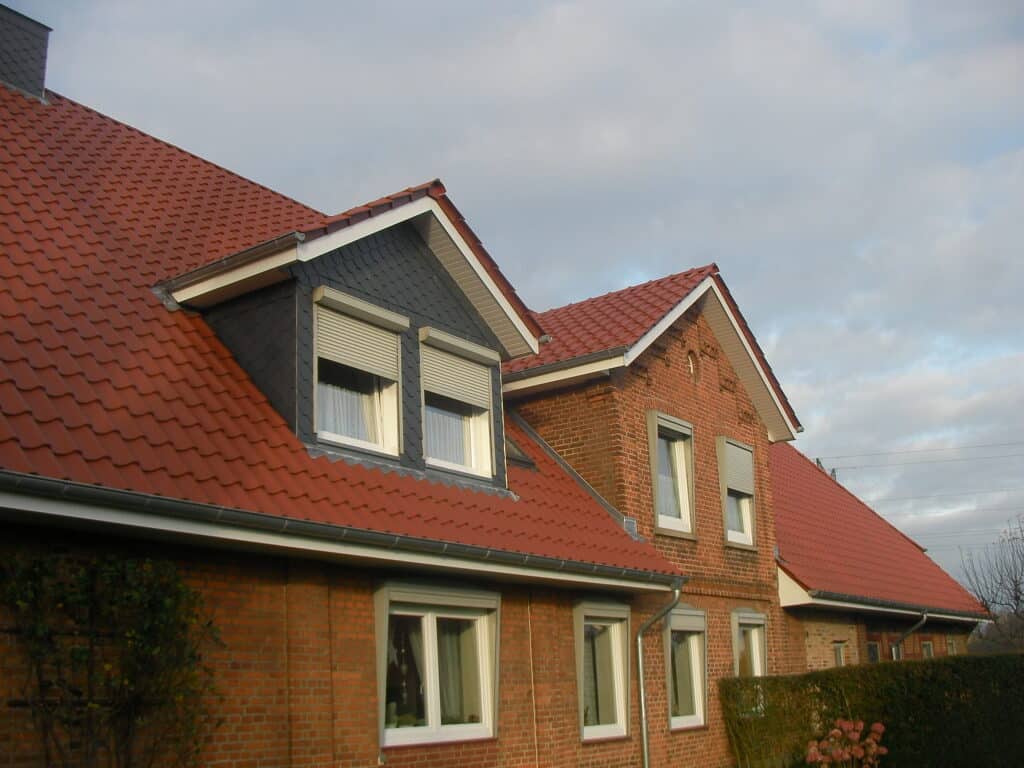 Rotes Ziegeldach eines Backsteinhauses mit verkleideter Giebelgaube und Zwerchgiebel.