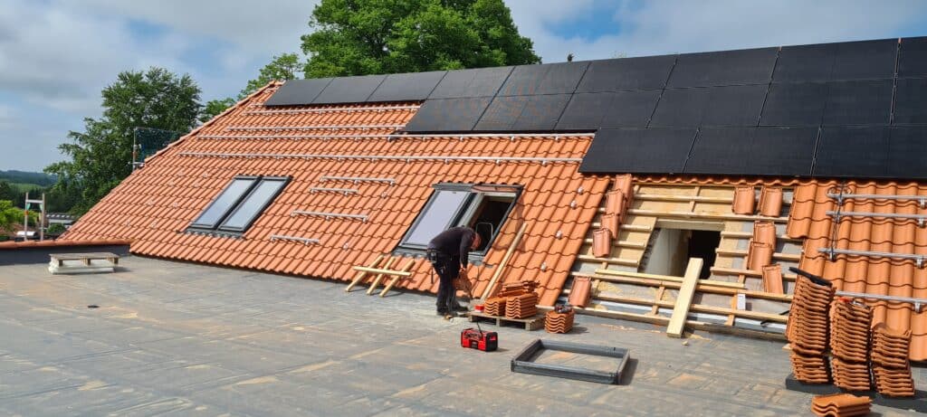 Arbeiten an Dachfenstern in einem roten Ziegeldach unterhalb einer Solaranlage.