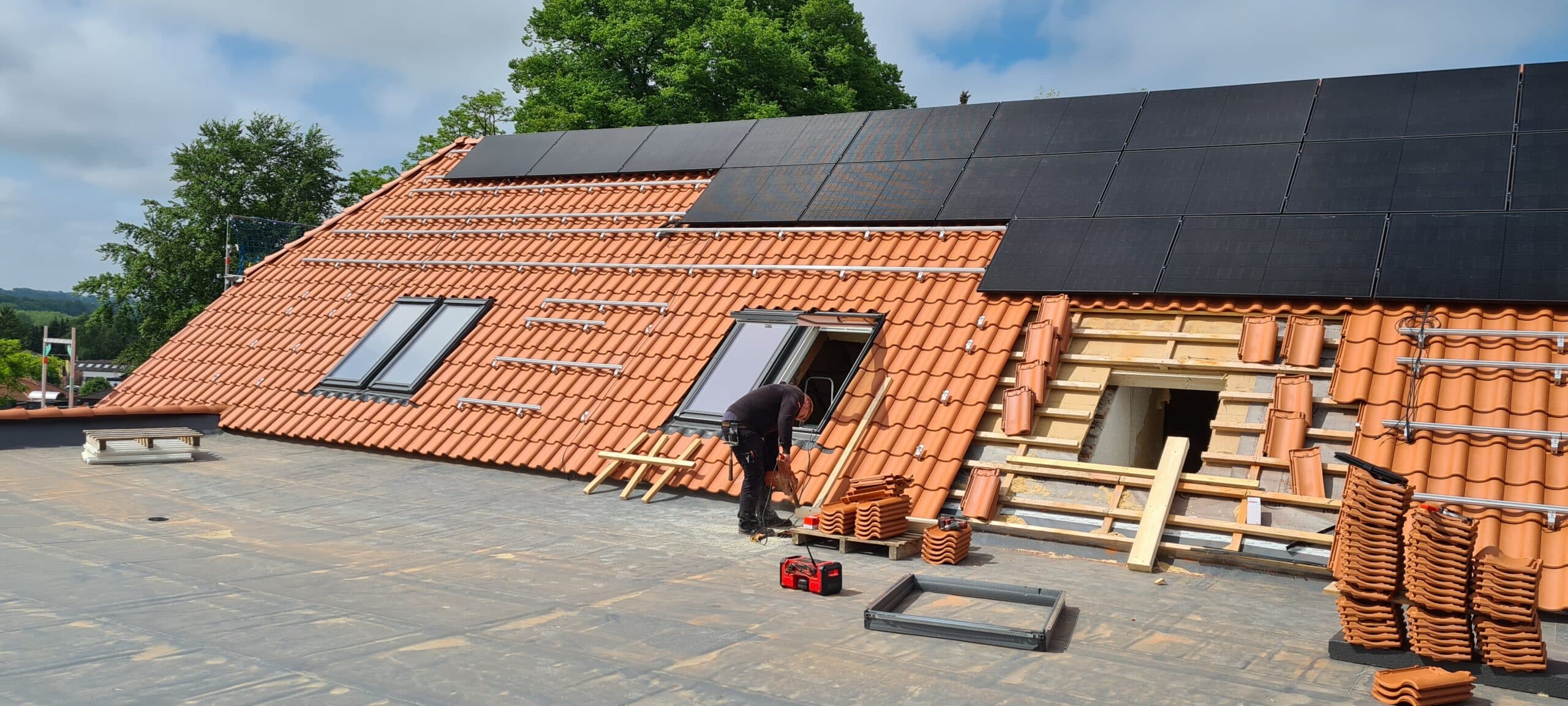 Arbeiten an Dachfenstern in einem roten Ziegeldach unterhalb einer Solaranlage.