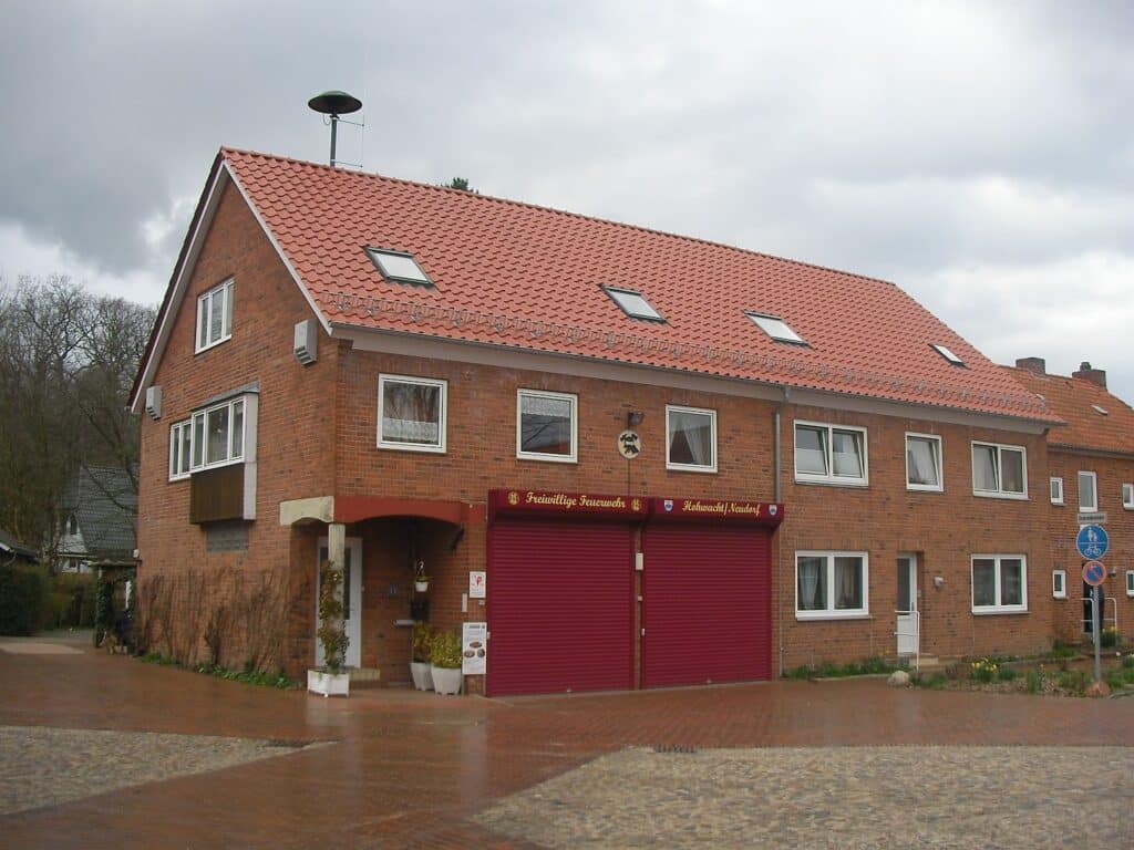 Backsteingebäude mit rotem Ziegeldach, mehreren Dachfenstern und großen roten Toren.