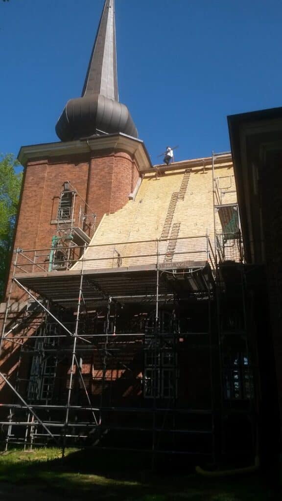 Eingerüstete Backsteinkirche mit Kirchturm und freigelegter Dachfläche während der Dacharbeiten.