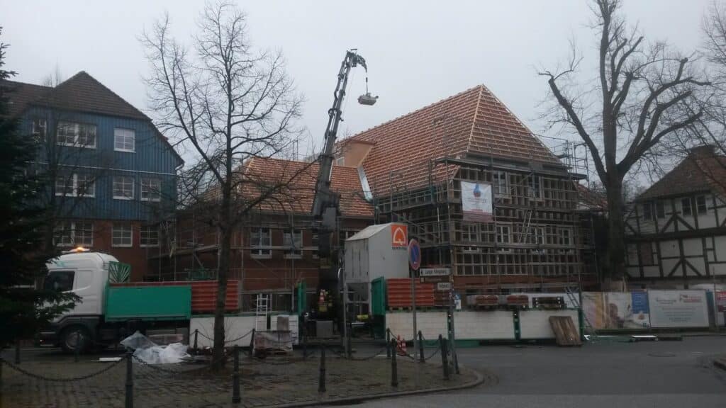 Eingerüstetes Fachwerkgebäude mit roter Dacheindeckung und einem Kran auf der Baustelle.