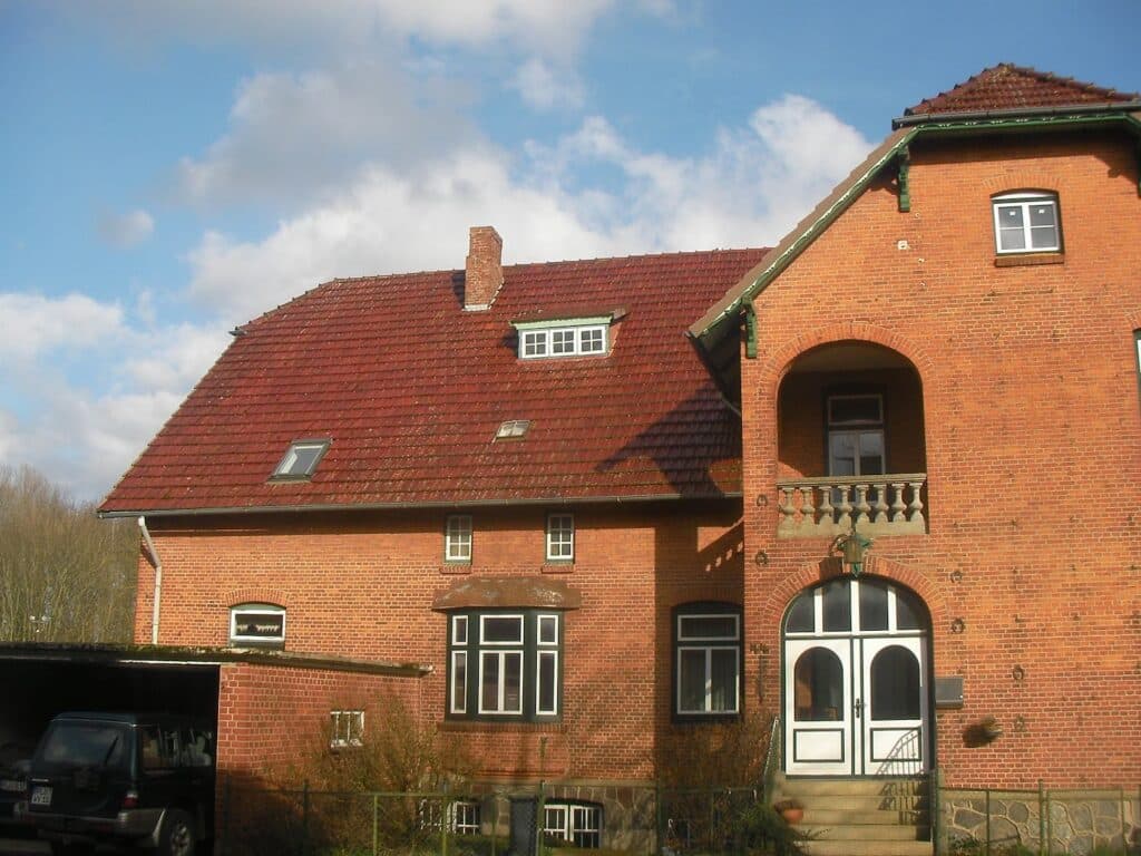 Backsteinhaus vor der Dachsanierung mit älterem roten Dach und einer kleinen Dachöffnung.