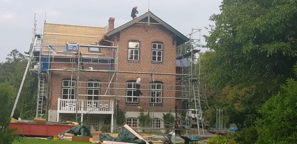 Eingerüstetes Backsteinhaus mit freigelegter Holzschalung während der Dachsanierung.