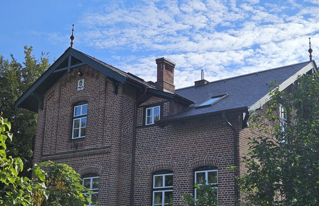 Historisches Backsteinhaus nach der Dachsanierung mit dunklem Naturschieferdach und Dachfenstern.