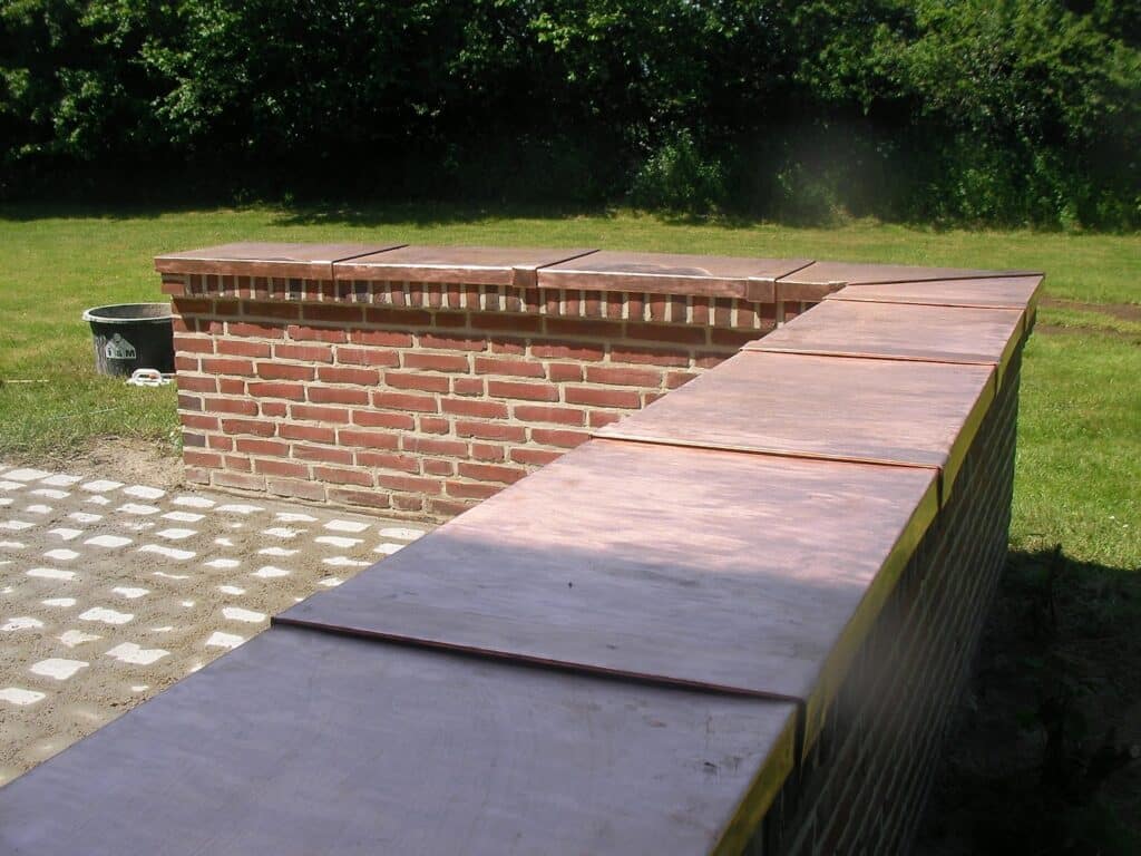 Nahansicht einer kupferfarbenen Mauerabdeckung mit überlappenden Verbindungen auf einer Backsteinmauer.