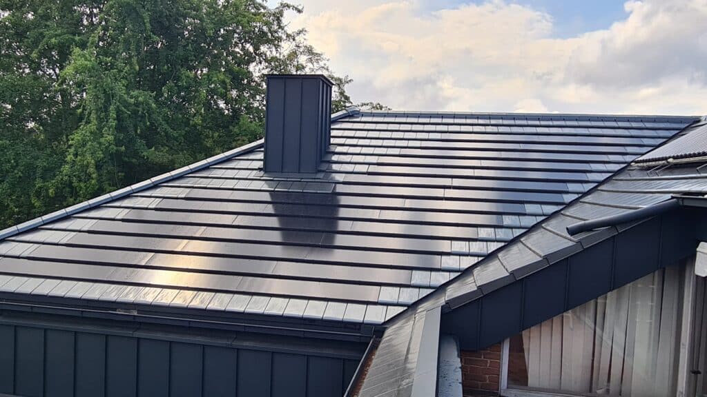 Dachintegrierte Photovoltaik auf einem dunklen Dach mit metallverkleidetem Schornstein.