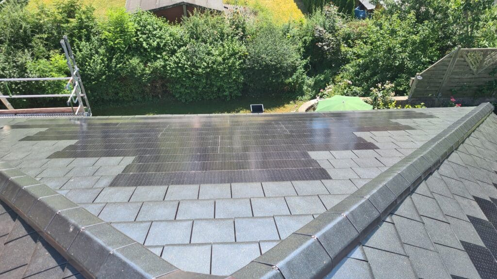Dunkle Photovoltaikelemente zwischen grauen Dachplatten auf einer geneigten Dachfläche.
