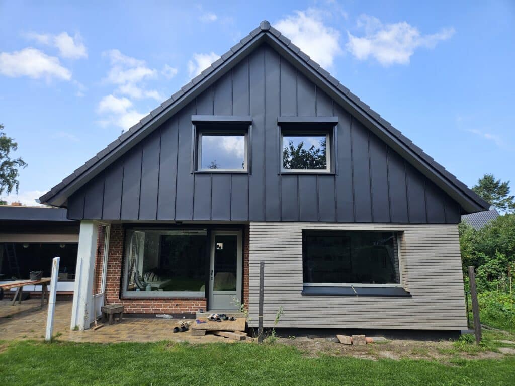 Hausgiebel mit dunkler senkrechter Metallverkleidung über einer hell verkleideten Fassade.