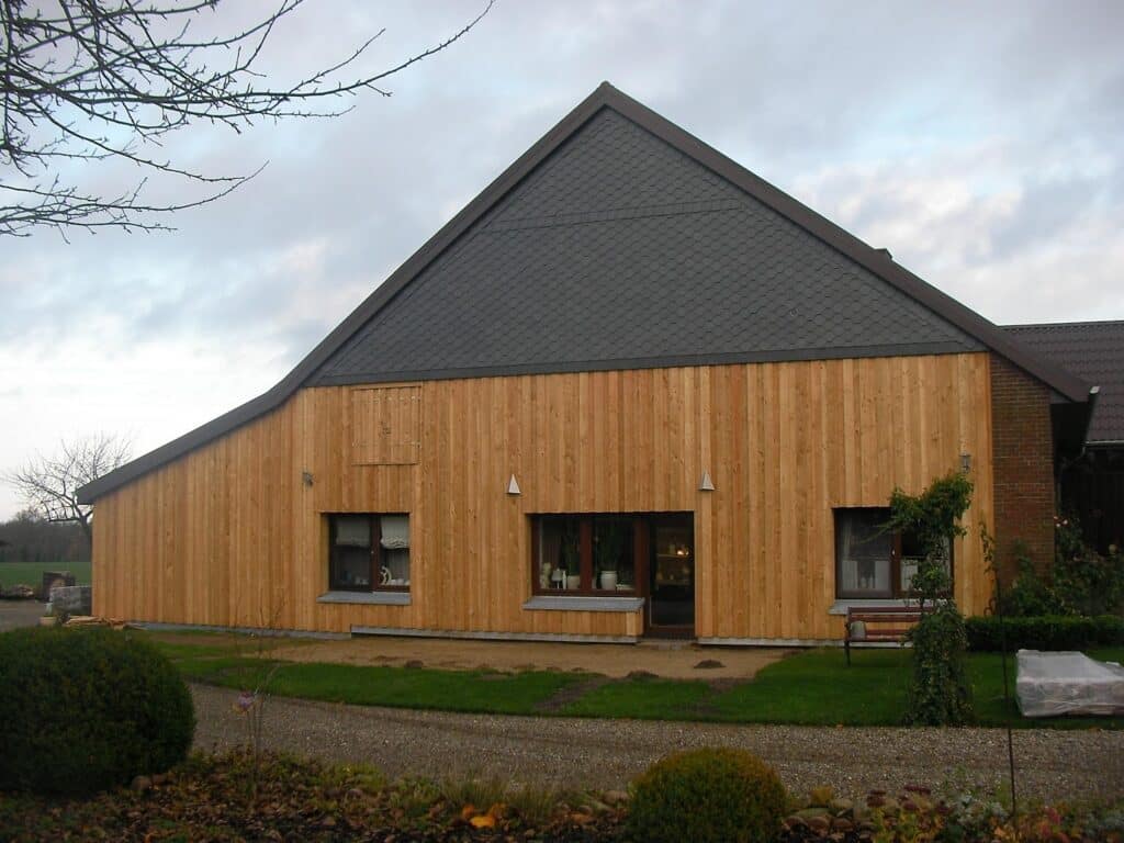 Gebäude mit senkrechter Holzfassade, dunkler Giebelverkleidung und drei Fenstern im Erdgeschoss.