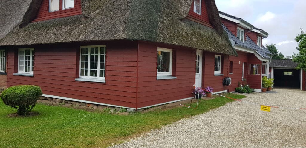 Reetgedecktes Haus mit roter waagerechter Fassadenverkleidung und weißen Fenstern.