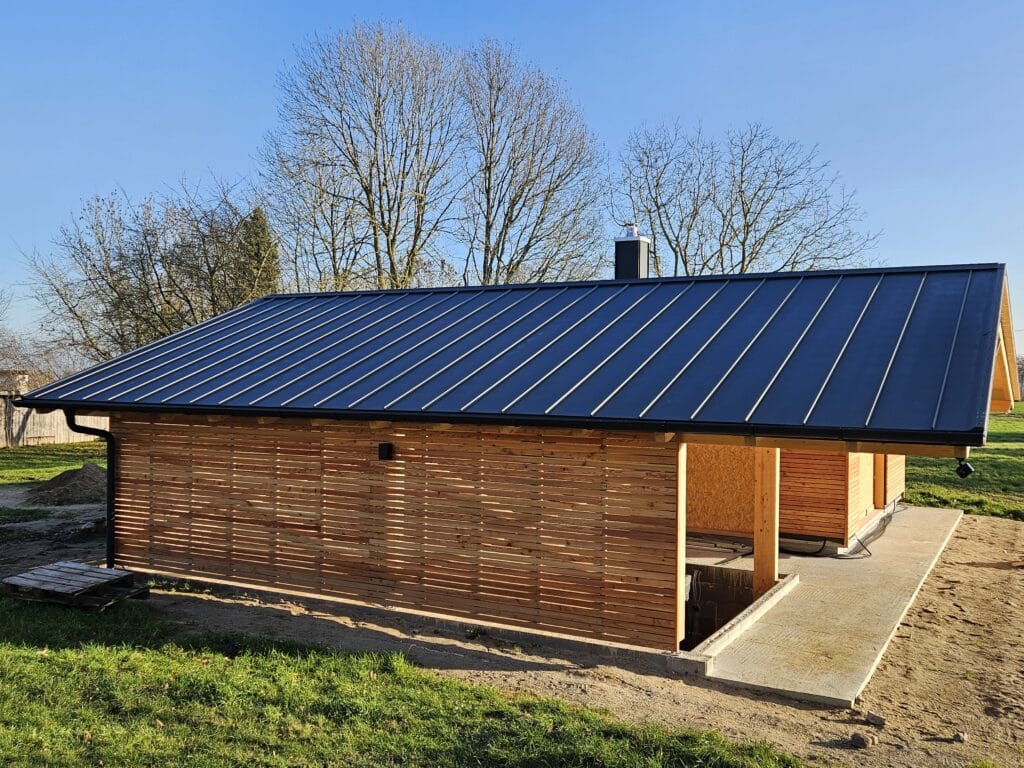 Carport mit dunklem Stehfalz-Metalldach, Dachüberstand und offenem seitlichen Unterstand.