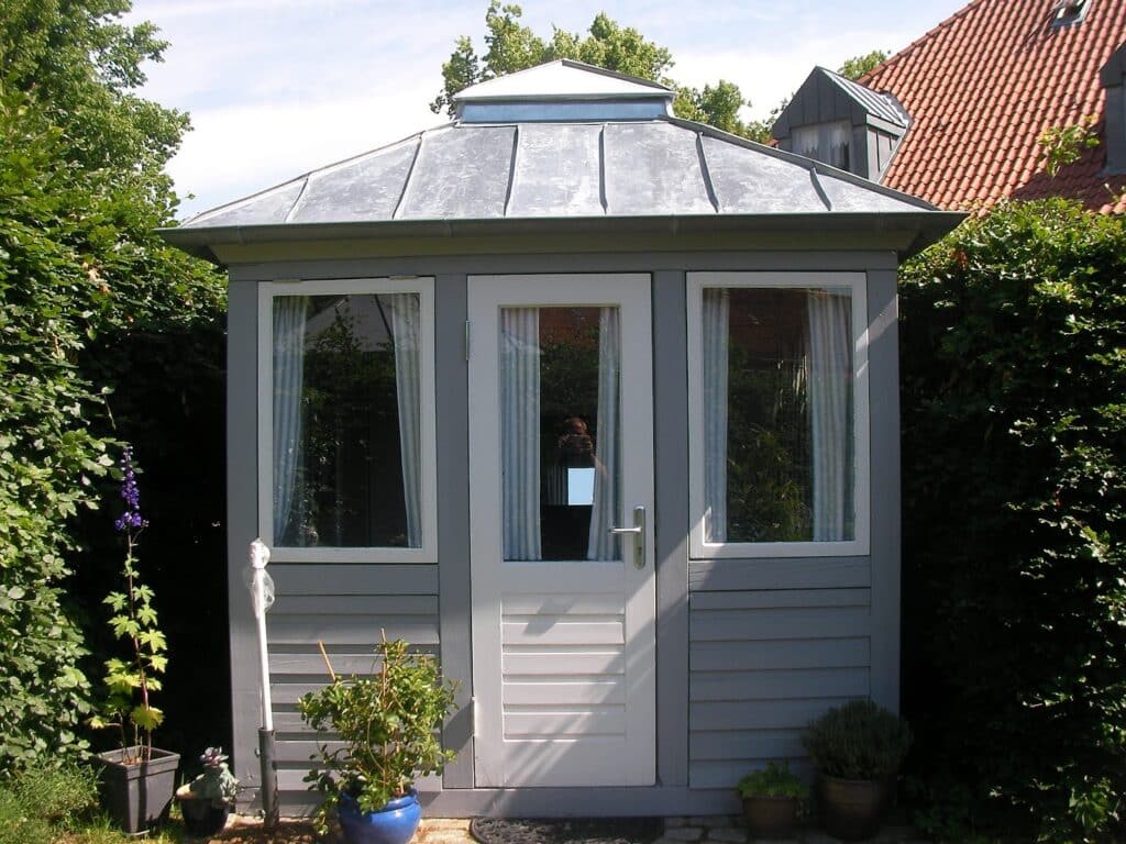 Weißer Gartenpavillon mit mehrseitigem Metalldach und sichtbaren Falzen.