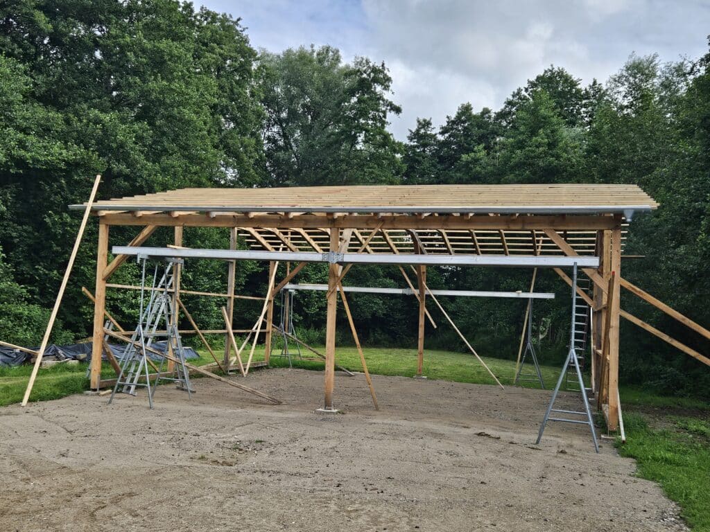 Offene Holzkonstruktion eines Unterstands mit Stützen, Dachbalken und provisorischen Aussteifungen.