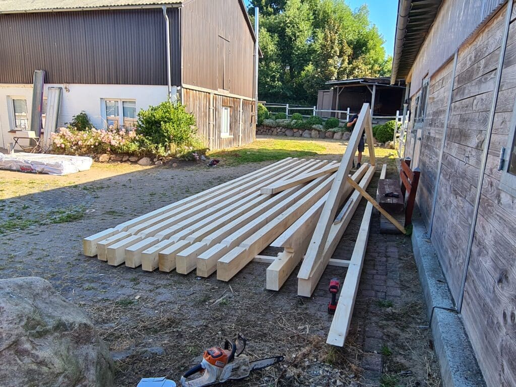 Lange bearbeitete Holzbalken liegen nebeneinander auf dem Betriebshof einer Zimmerei.