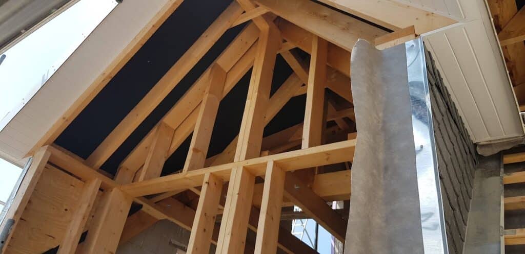 Offene Holzkonstruktion einer Gaube mit sichtbaren Sparren, Stützen und Anschlüssen.