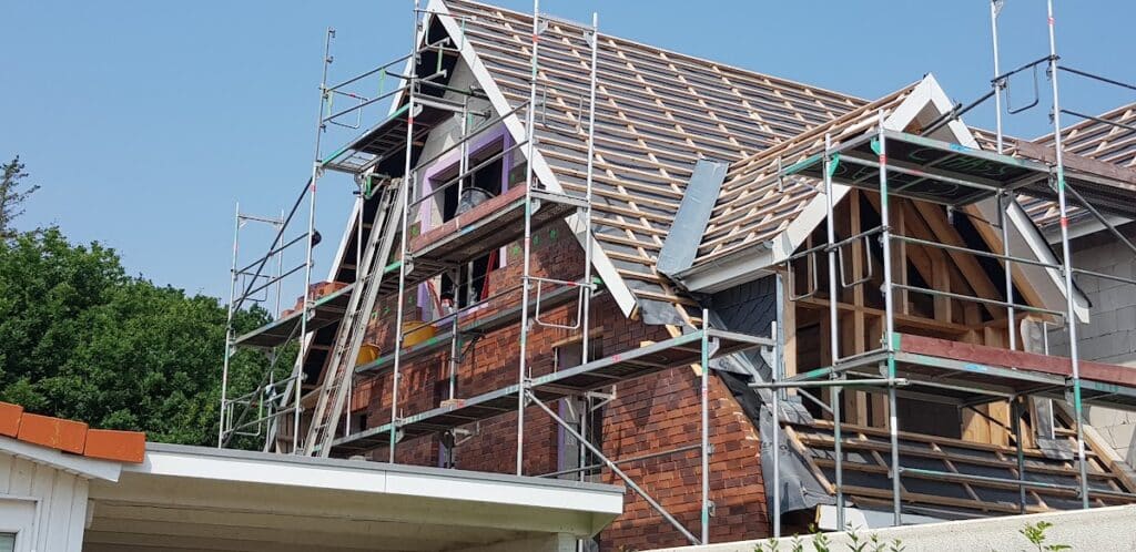 Eingerüstetes Haus mit sichtbarer Dachlattung und Holzkonstruktion an der Giebelseite.